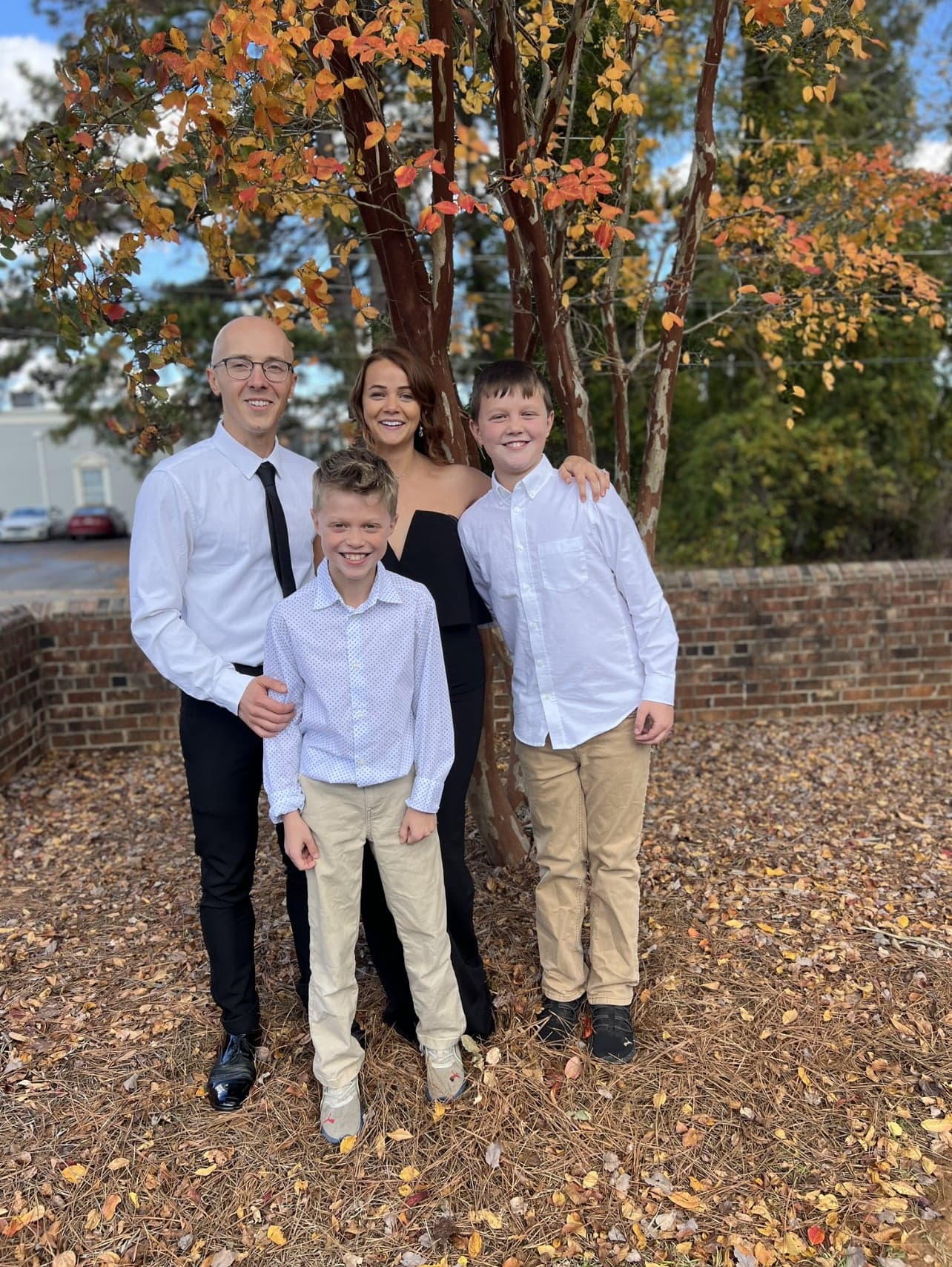 Derek with his wife and their two sons, standing under a tree with fall leaves